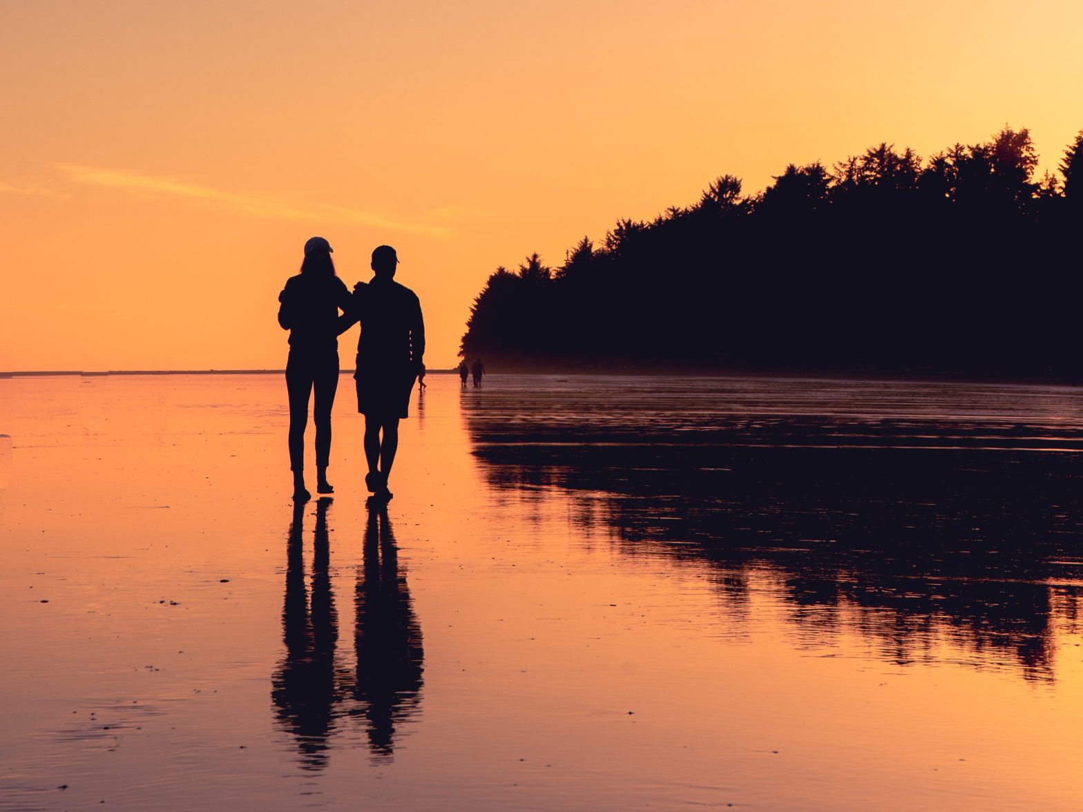 Two people walking side by side on the beach at sunset.